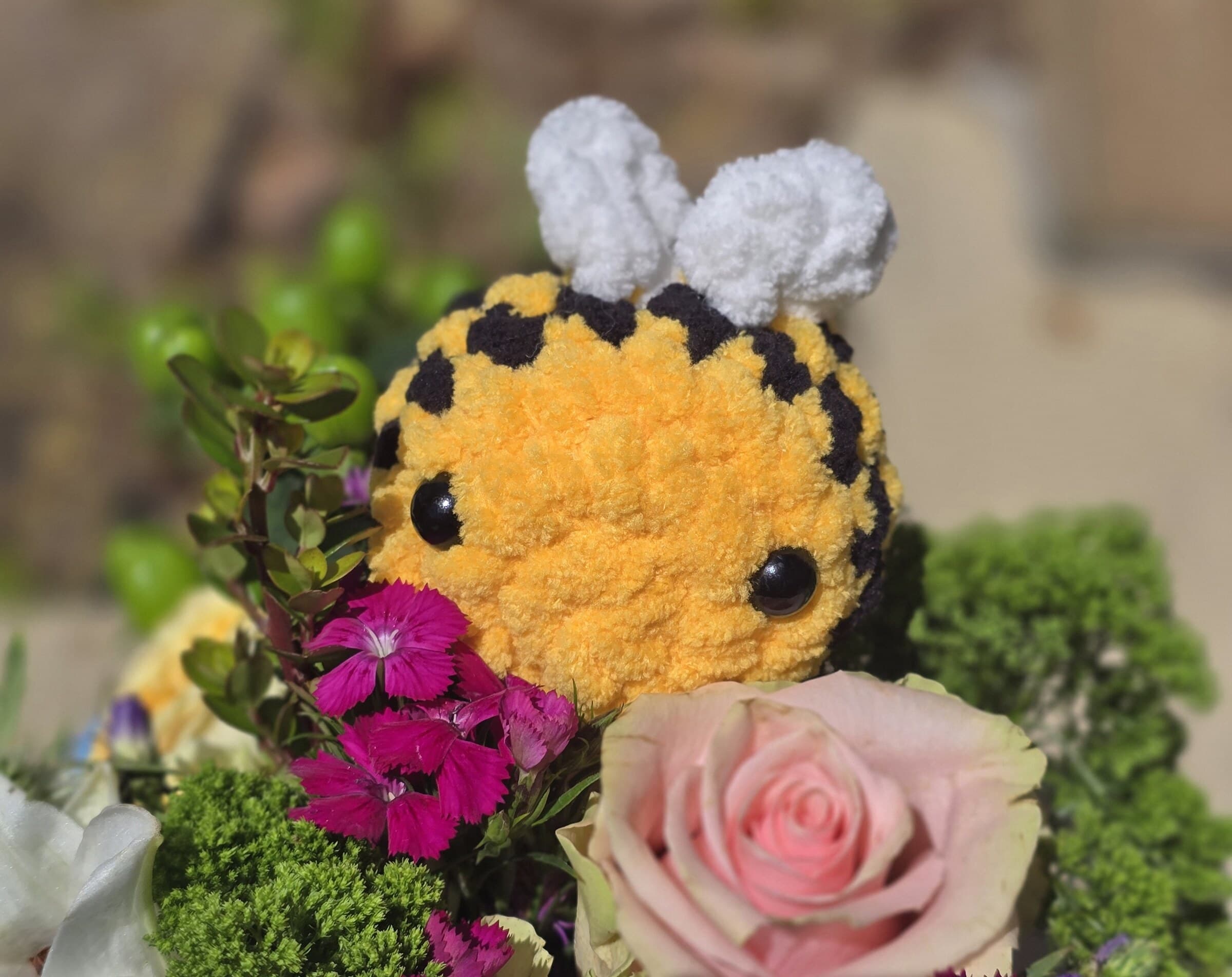 A yellow and black crocheted bee plushie nestled among pink and white flowers.