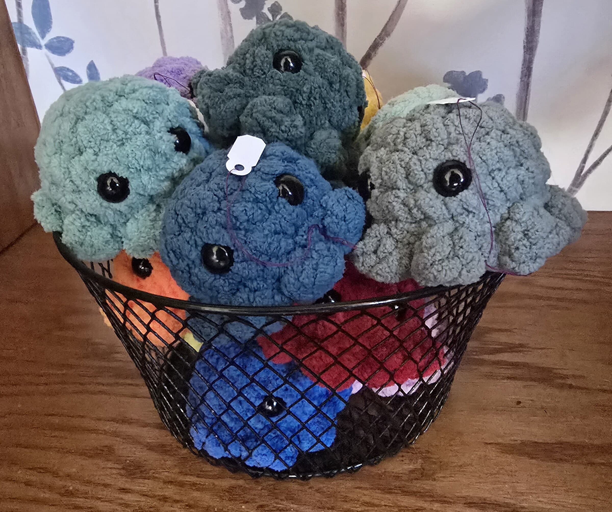 A wire basket full of mini crocheted octopus plushies in blue, gray, and teal.