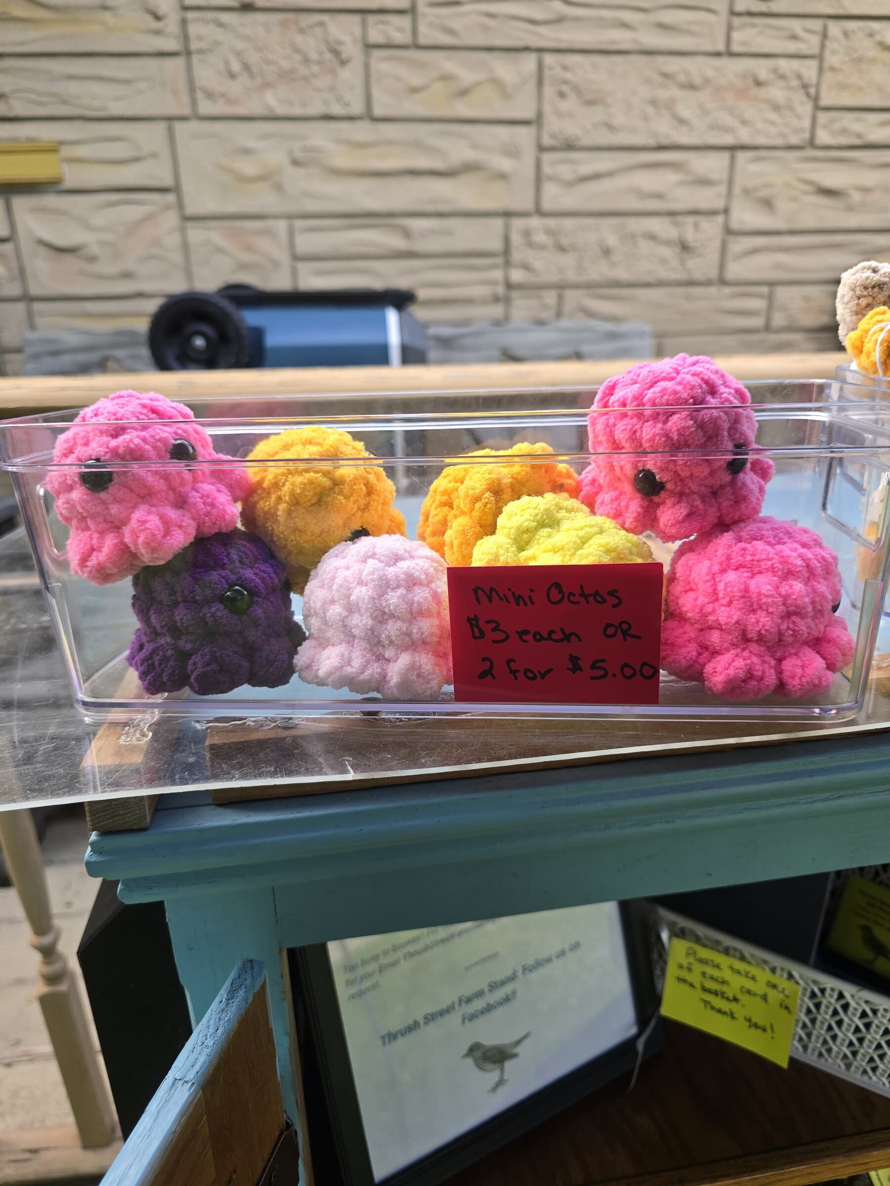 Pink mini crocheted octopus plushies displayed in a basket at the farm stand.