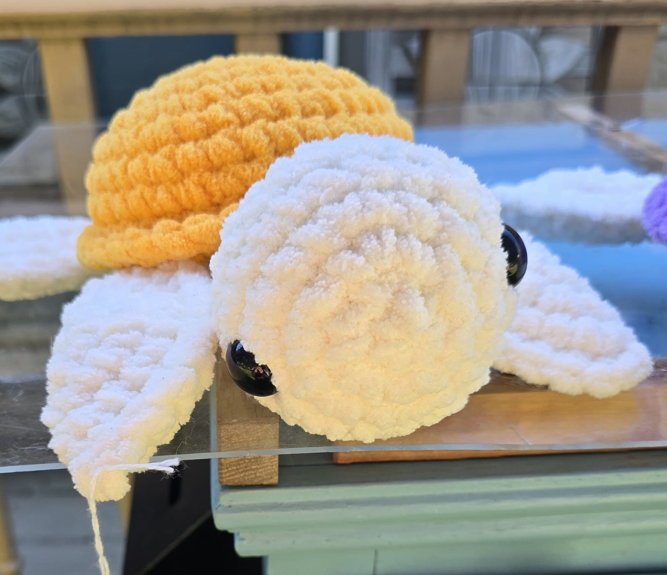 A yellow and white crocheted turtle plushie resting on the farm stand counter.